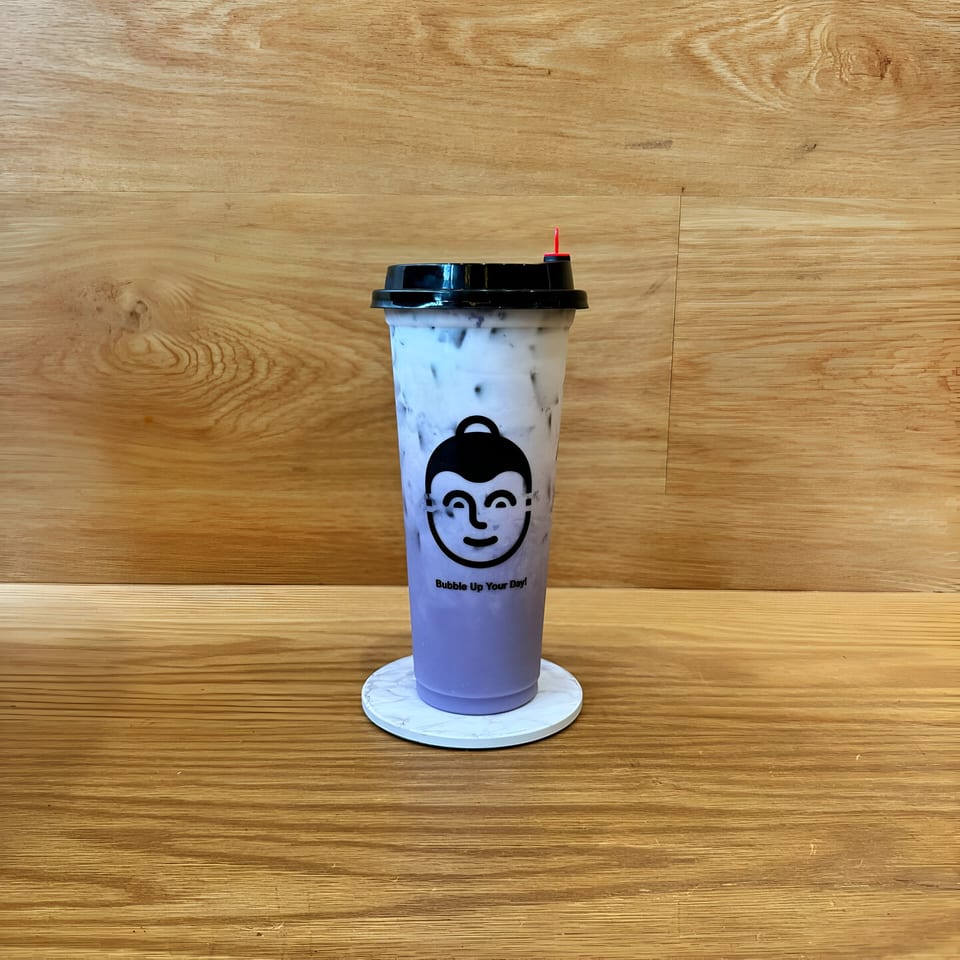 Koo Thai taro bubble tea with a black lid and red stopper on a marble coaster.