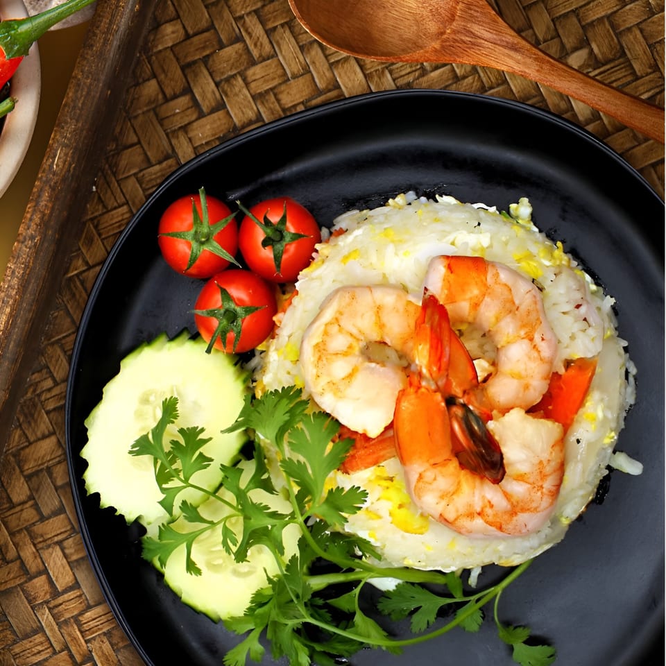 Koo Thai's shrimp fried rice with cherry tomatoes, cucumber slices, and cilantro on a black plate.