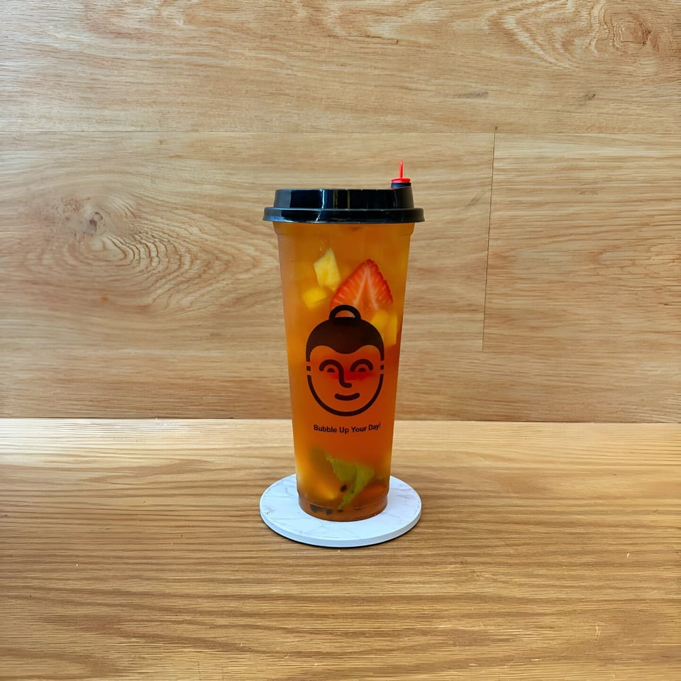 Koo Thai fruit tea with strawberries and mango, on a white coaster against a wooden background.