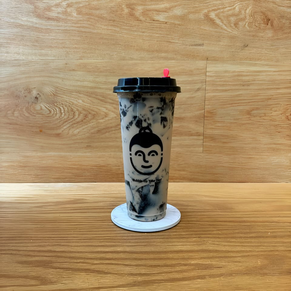Koo Thai bubble tea with a black lid and red heart stopper on a white coaster.