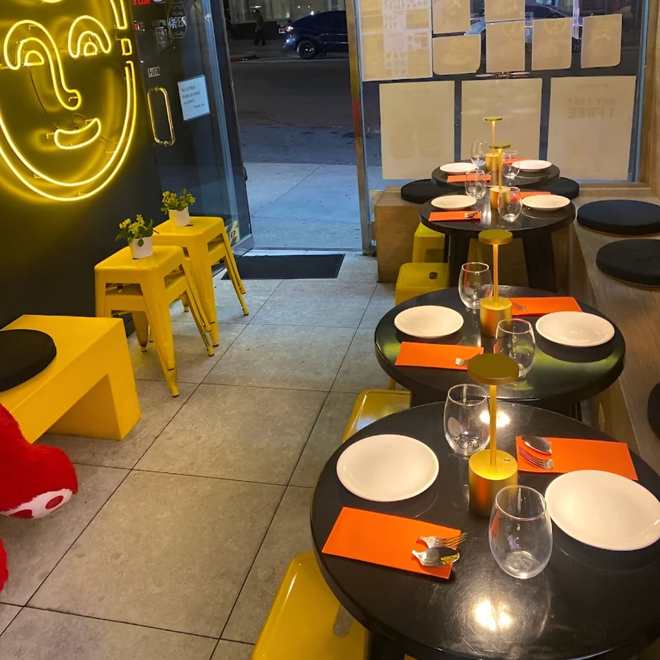 Koo Thai restaurant interior with neon yellow decor, black tables, white plates, and orange placemats.