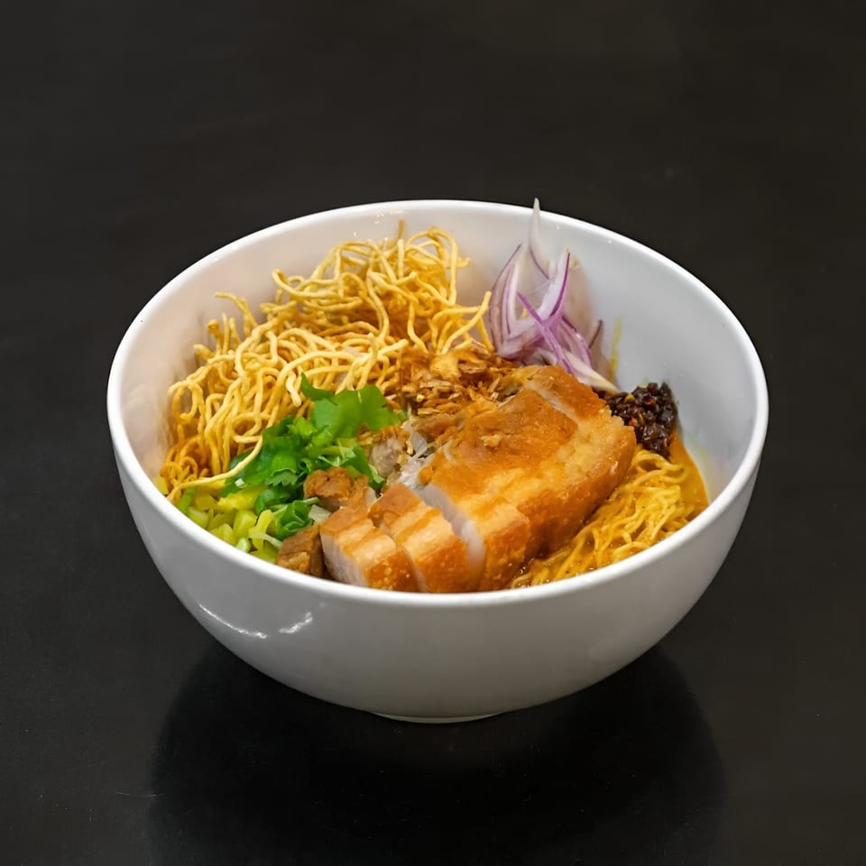 Koo Thai's Khao Soi with crispy pork belly, egg noodles, red onion, and cilantro in a white bowl.