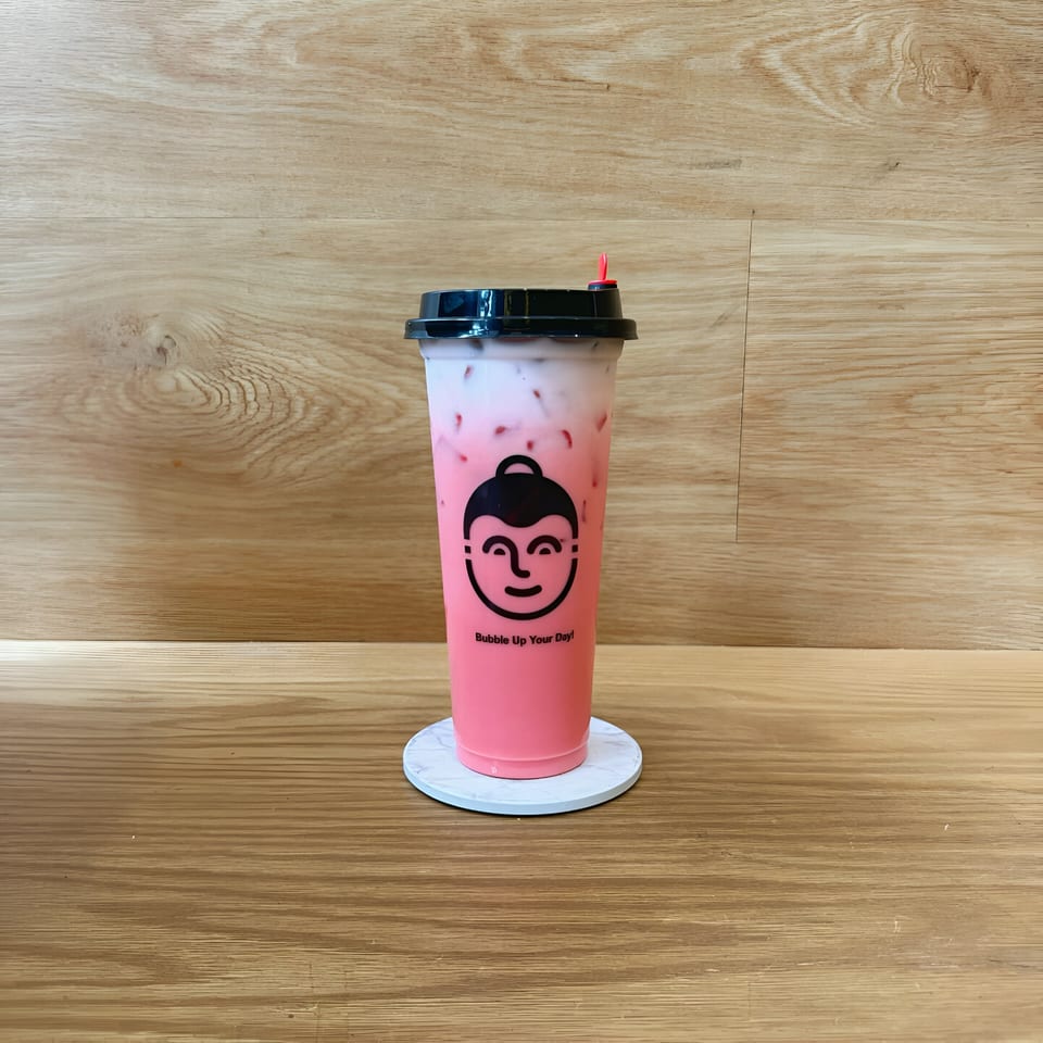 Pink and white Thai iced tea with a black logo and red straw, on a wooden table.