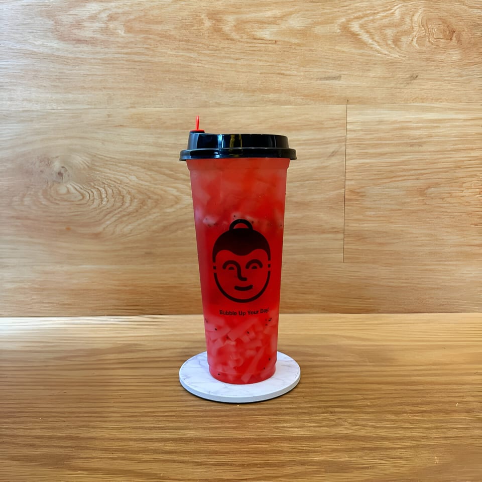 Koo Thai's red bubble tea with fruit pieces and black seeds, on a white coaster.