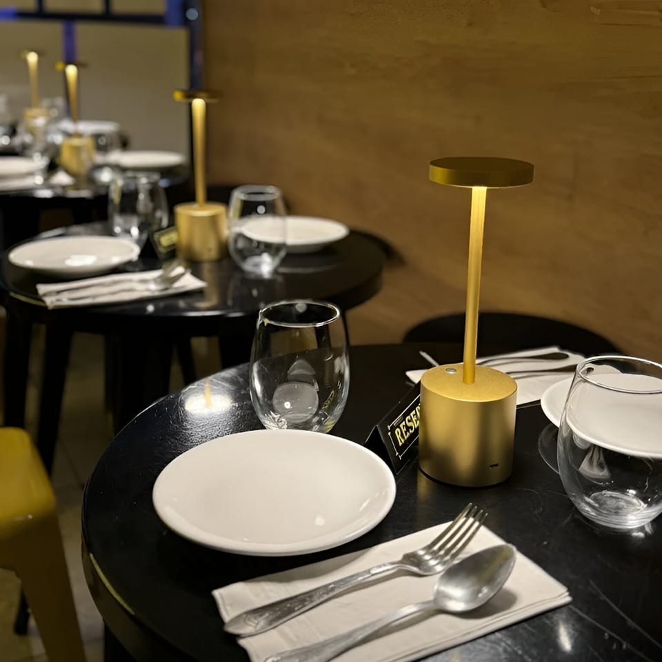 Set tables with white plates, silverware, glasses, and golden lamps create an inviting ambiance at Koo Thai.